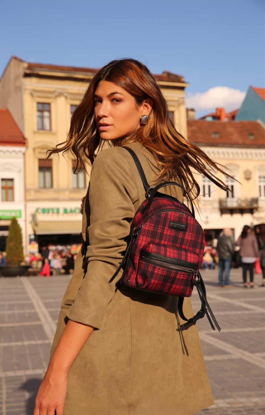 Modelo em cenário urbano usando looks com mochila junto com um casaco bege